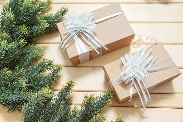 Square craft gifts boxes with fir branches on a wooden background. Light brown cardboard boxes with white ribbons and bows Christmas gifts. Gifts for the new year