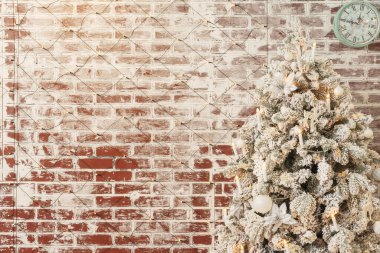 Çelenklerle kaplı bir duvarın arkasında karla kaplı bir Noel ağacı. Kar fotoğrafı stüdyosu olan beyaz sahte Noel ağacı. Beyaz süslemeleri ve mum şeklinde çelenkleri olan güzel Noel ağacı.
