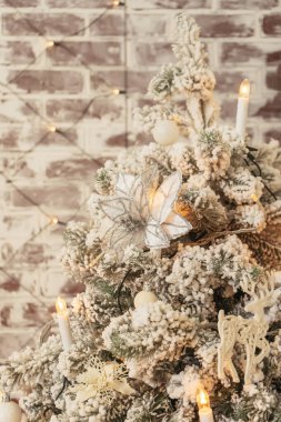 Karla kaplı bir Noel ağacında mum şeklinde çelenkler. Beyaz gümüş süsleri noel ağacında kar taneleri. Tuğla bir duvarın arkasında karlı bir Noel ağacı