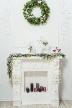 Şöminedeki iki beyaz noel geyiği figürü. Noel geyiği ve köknar dallarıyla şömine dekorasyonu. Şöminenin üzerinde pembe koni olan Noel çelengi.