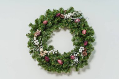 Beyaz böğürtlenli sahte ladin çelengi ve duvarında pembe bordo parlak koni Noel süsleri. Ev stüdyosunda Noel 'in detaylarını anlatıyor. Beyaz arka planda Noel çelengi
