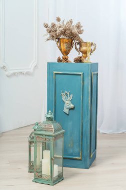 Mavi büfe sütunu, sıva ve bir buket kozalaklı altın vazolar. Metal fener tutacakları ve mumlar Noel süslemeleri. Odanın yeni yıl için klasik bir tasarımı.