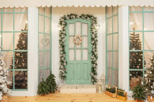 圣诞装饰品和圣诞树上有绿色门的门廊 斯普鲁斯在门的周围挂着花环 房子漂亮的冬季露台 有复古灯泡的花环 — 图库照片