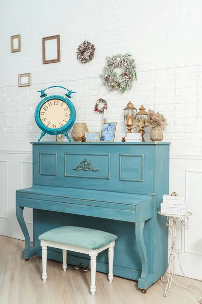 Blue piano with Christmas decor wreaths on the wall. Large clock alarm clock on piano new year decor. The room is decorated in a classic style with a piano and a Christmas tree in blue and gold style