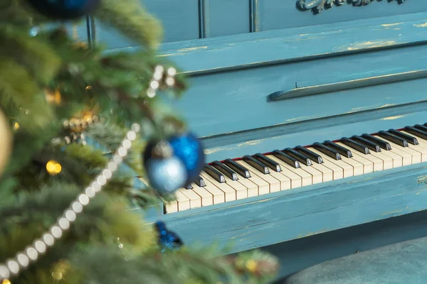 Piano close-up with Gold and blue balloons on a Christmas tree close-up in the foreground. Christmas decorations on Christmas trees balls garlands and beads. Blue and gold decoration of the new year home interior