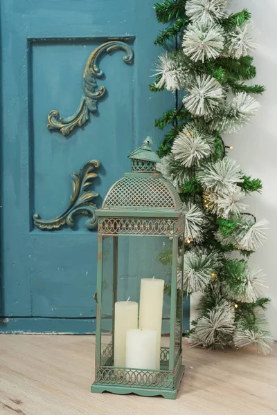 Vintage metal lantern candle holder with white candles inside. Christmas candle holder stylized as a copper Oriental motif on the background of a blue door. Lantern candle holder in the interior