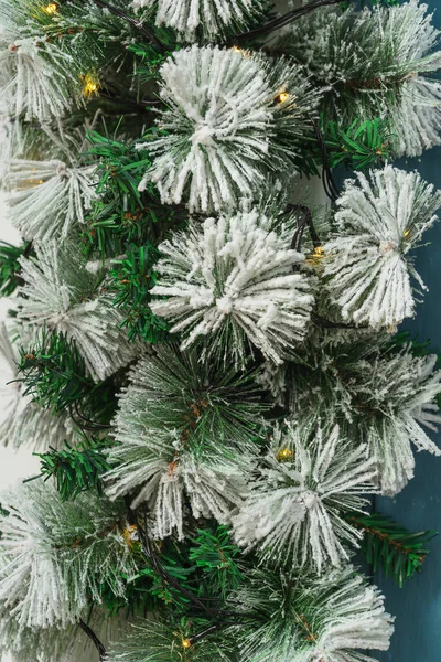 Artificial spruce pine garland with snow close-up. Christmas snow-covered fir garland with lights. Christmas home decoration texture of green fir garland