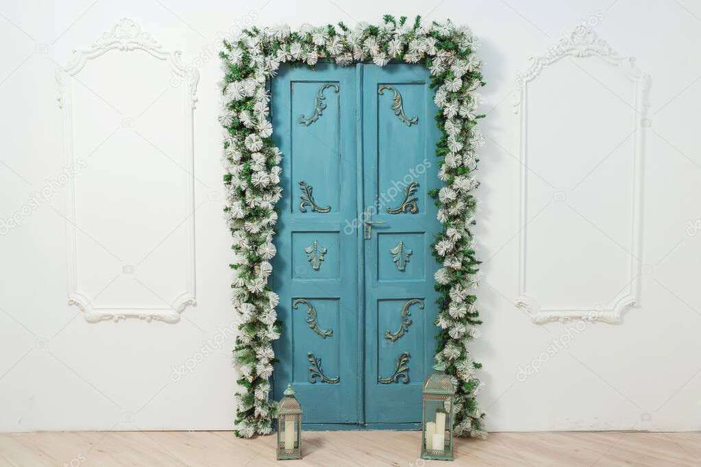 Blue door with stucco and fir garlands Christmas decorations. The design of the room in a classic style for the new year. Pine fir artificial garlands around the door and metal lanterns candlesticks Studio decoration