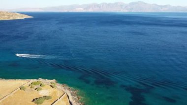 Koyu mavi bir denizde hız yapan bir motorlu teknenin hava görüntüsü. Spinalonga Adası, Girit, Yunanistan