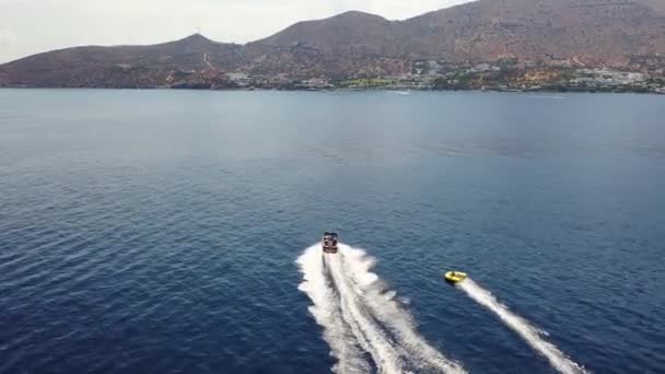 Vue aérienne d'un bateau à moteur remorquant un tube. Elounda, Crète, Grèce — Video