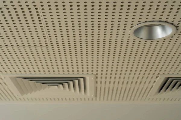 Kanal ızgaraları ve ışıkları olan beyaz ses emici tavan.