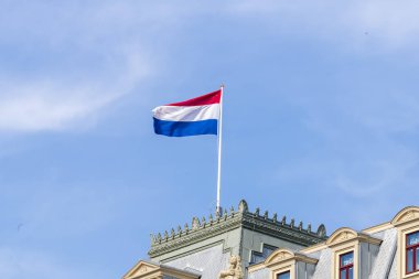 Hollanda Krallığı bayrakları kırmızı, beyaz ve mavi kumaş şeritleriyle bir binanın bayrak direğine bağlanmış ve rüzgarda dalgalanıyor..