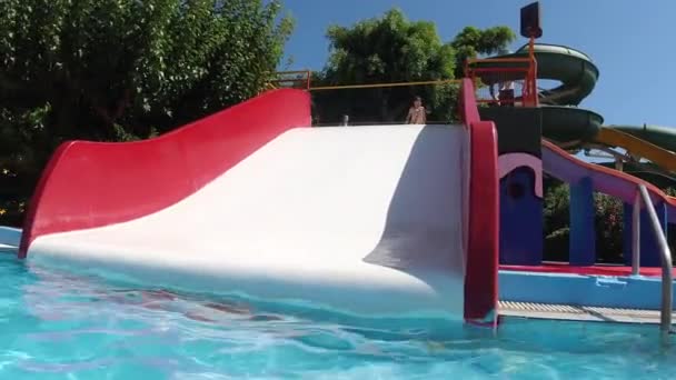 Niña feliz divirtiéndose con tobogán de agua en una piscina disfrutando de una excursión de un día a un parque de atracciones acuático durante las vacaciones familiares de verano — Vídeo de stock