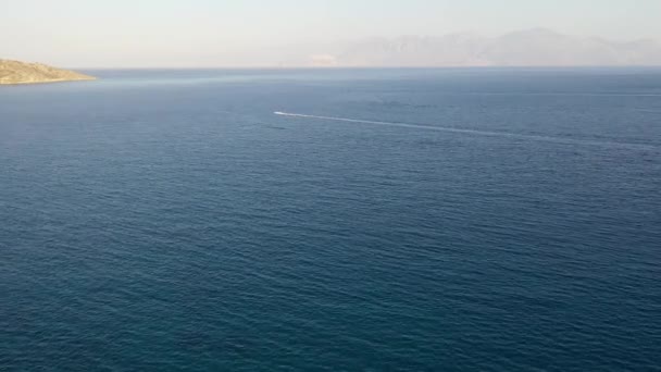 Vista aérea de un barco de motos acuáticas en un mar de color azul profundo. Isla Spinalonga, Creta, Grecia — Vídeos de Stock