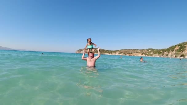Mutlu aktif aile, genç baba ve tatlı kızı, sevimli kız, Akdeniz 'de oynuyorlar, Yunanistan' ın Girit kentindeki güzel bir tropikal ada beldesinde yavaş çekimde suya atlıyorlar. — Stok video