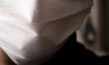 Tıbbi ya da cerrahi maske takan genç bir adamın yüzüyle yakın çekim.