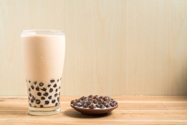 Bir bardak inci sütlü çay (köpüklü çay olarak da bilinir) ve ahşap zemin üzerinde bir tabak tapyoka topu. İnci sütlü çay Tayvan 'daki en temsili içecektir. Tayvan yemeği. Kopyalama alanı ile.