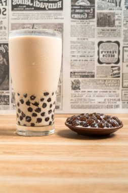 Bir bardak inci sütlü çay (köpüklü çay olarak da bilinir) ve ahşap zemin üzerinde bir tabak tapyoka topu. İnci sütlü çay Tayvan 'daki en temsili içecektir. Tayvan yemeği. Kopyalama alanı ile.