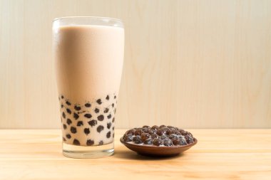 Bir bardak inci sütlü çay (köpüklü çay olarak da bilinir) ve ahşap zemin üzerinde bir tabak tapyoka topu. İnci sütlü çay Tayvan 'daki en temsili içecektir. Tayvan yemeği. Kopyalama alanı ile.