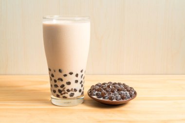 Bir bardak inci sütlü çay (köpüklü çay olarak da bilinir) ve ahşap zemin üzerinde bir tabak tapyoka topu. İnci sütlü çay Tayvan 'daki en temsili içecektir. Tayvan yemeği. Kopyalama alanı ile.