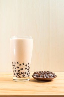 Bir bardak inci sütlü çay (köpüklü çay olarak da bilinir) ve ahşap zemin üzerinde bir tabak tapyoka topu. İnci sütlü çay Tayvan 'daki en temsili içecektir. Tayvan yemeği. Kopyalama alanı ile.