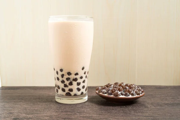 A glass cup of pearl milk tea (also called bubble tea) and a plate of tapioca ball on wooden background. Pearl milk tea is the most representative drink in Taiwan. Taiwan food . With copy space.