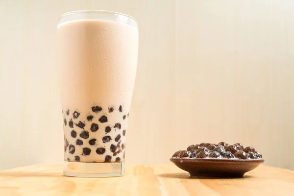 A glass cup of pearl milk tea (also called bubble tea) and a plate of tapioca ball on wooden background. Pearl milk tea is the most representative drink in Taiwan. Taiwan food . With copy space.