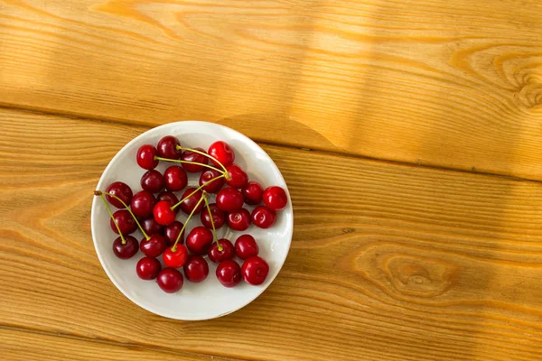 Reife rote Kirschen auf einem Teller auf einem hölzernen Hintergrund. Früchte auf braunem Holzgrund. — Stockfoto