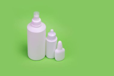 Yeşil arka planda üç beyaz şişe. Cilt bakımı için makyaj seti. Farklı boyutlarda şişeler..