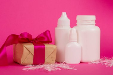 Kozmetik ürünleri ve pembe kurdeleli hediye. Pembe arka planda beyaz şişeler. Pembe arka planda kozmetik seti.