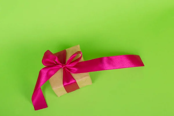 Conceito do dia das mulheres. Caixa de presente embrulhada em papel artesanal. presente com uma fita rosa em um fundo verde . — Fotografia de Stock
