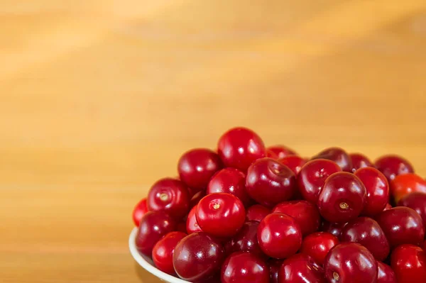 Cerezas rojas maduras sobre un fondo de madera. Bayas rojas en un plato sobre un fondo marrón . — Foto de Stock