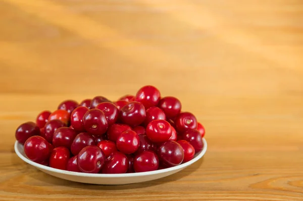 Dojrzałe czerwone wiśnie na drewnianym tle. Czerwone jagody na talerzu na brązowym tle. — Zdjęcie stockowe