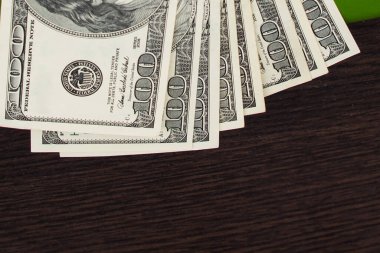 Kahverengi arka planda parası olan bir cüzdan. Cüzdanında bir paket dolar var. Banknotlar 100 dolar.