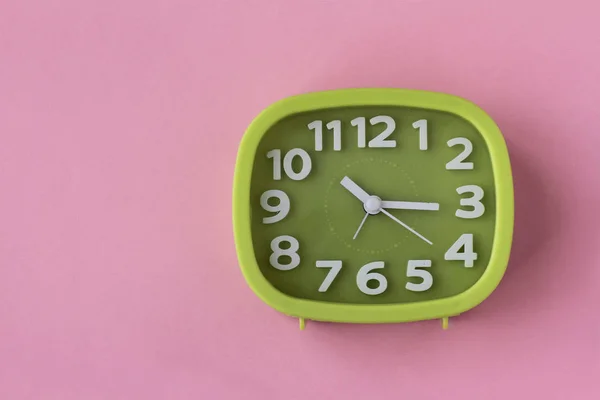 粉红色背景上有白色数字和箭头的绿色时钟 — 图库照片