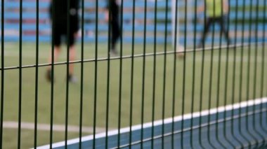 Gençler çocuklar ile silah, güvenlik, defocused çit odaklanmak için çit çit futbol sahasında futbol oynar