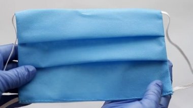 Doktorun eldiveni ağız ve burnu kapamak için tipik tek kullanımlık ameliyat maskesini tutuyor. Anti virüs koruması Coronavirus, COVID-19 ve diğer tehlikeli virüsler. Tam HD biçimi