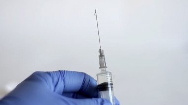 Doktorun elleri mavi tıbbi eldivende bir şırınga tutuyor. Şırınganın içinden ilaçla hava salıyor ve enjeksiyona hazır. Coronavirus, COVID-19 ve diğer virüslerin korunması için sağlık ve tıbbı kavramsallaştır.