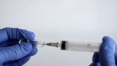 Doktorun elinde mavi tıbbi eldiven var ve ampulden tıbbi şırınga enjekte ediliyor. Coronavirus, COVID-19 ve diğer tehlikeli virüslerin korunması için sağlık ve tıbbı kavramsallaştır.