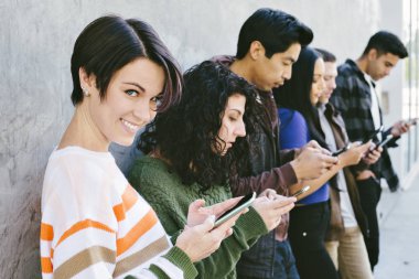 Çekici kız, arkadaşlarıyla birlikte teknoloji bağımlılığı olan cep telefonlarını gündüz vakti kullanırken kameraya bakıyor.
