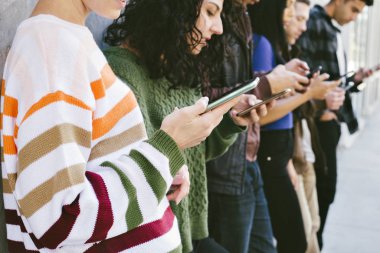 Genç erkekler ve kadınlar şehirdeki duvara dayanmış akıllı telefonlarına bakarlar. Teknoloji saplantısı kavramı.