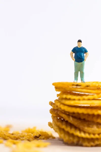 Miniature people, Fat man standing on potato chips on white background (food concept)