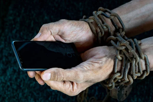 man hands tied with metallic chain with padlock on dark background suggesting internet or social media addiction