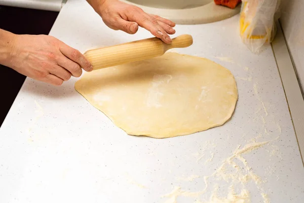 Saca la pasta. panadero lanza la masa en una mesa de cocina de madera espolvoreada con harina —  Fotos de Stock