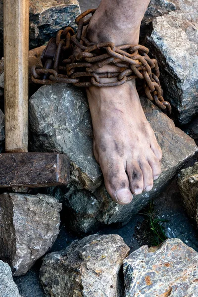 Sucio esclavo piernas en cadenas entre las piedras. Esclavo en un intento de liberarse. El símbolo del trabajo esclavo —  Fotos de Stock