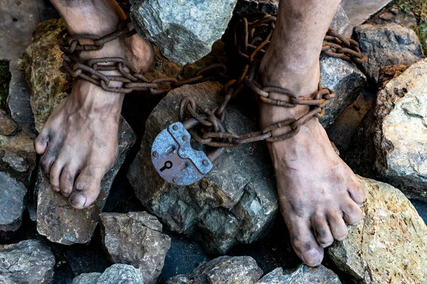 Dirty slave legs in chains among stones. Slave in an attempt to free himself. The symbol of slave labor