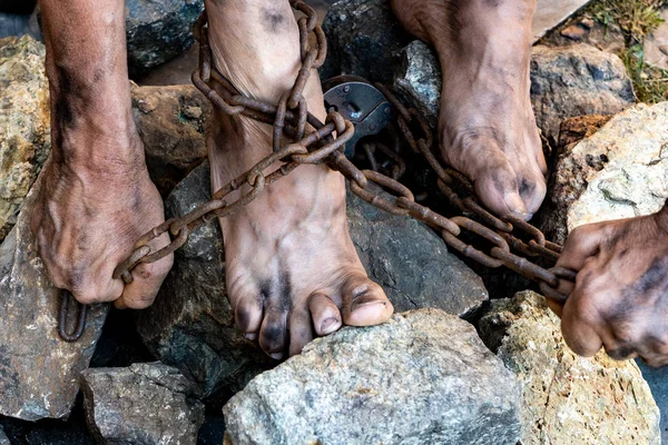 Brudne nogi niewolnika w łańcuchach między kamieniami. Niewolnik próbujący się uwolnić. Symbol niewolniczej pracy. — Zdjęcie stockowe