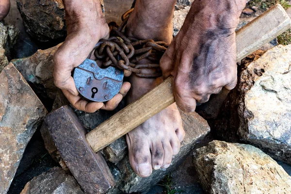 Las manos sucias de un esclavo sostienen un martillo entre las piedras. Esclavizar trabajos forzados en las canteras. El símbolo del trabajo esclavo . —  Fotos de Stock