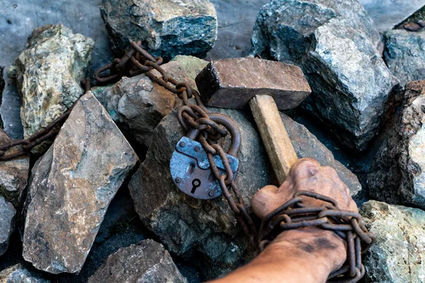 The dirty hands of a slave hold a hammer among the stones. Slave hard labor in the quarries. The symbol of slave labor.