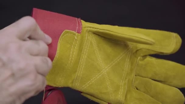 作業用手袋を着用する 暗い背景に男のクローズアップの手 ラフなスエードで作られた大きな作業新しい手袋 特殊溶接手袋 — ストック動画